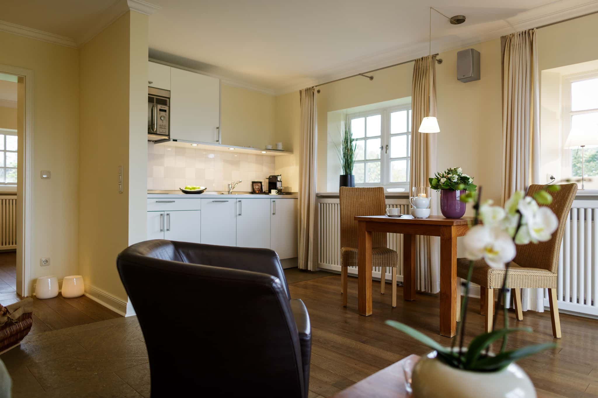 Wohnküche mit weißer Küchenzeile und Esstisch mit Korbstühlen im Appartement Meerlavendel im Lüüvhoog