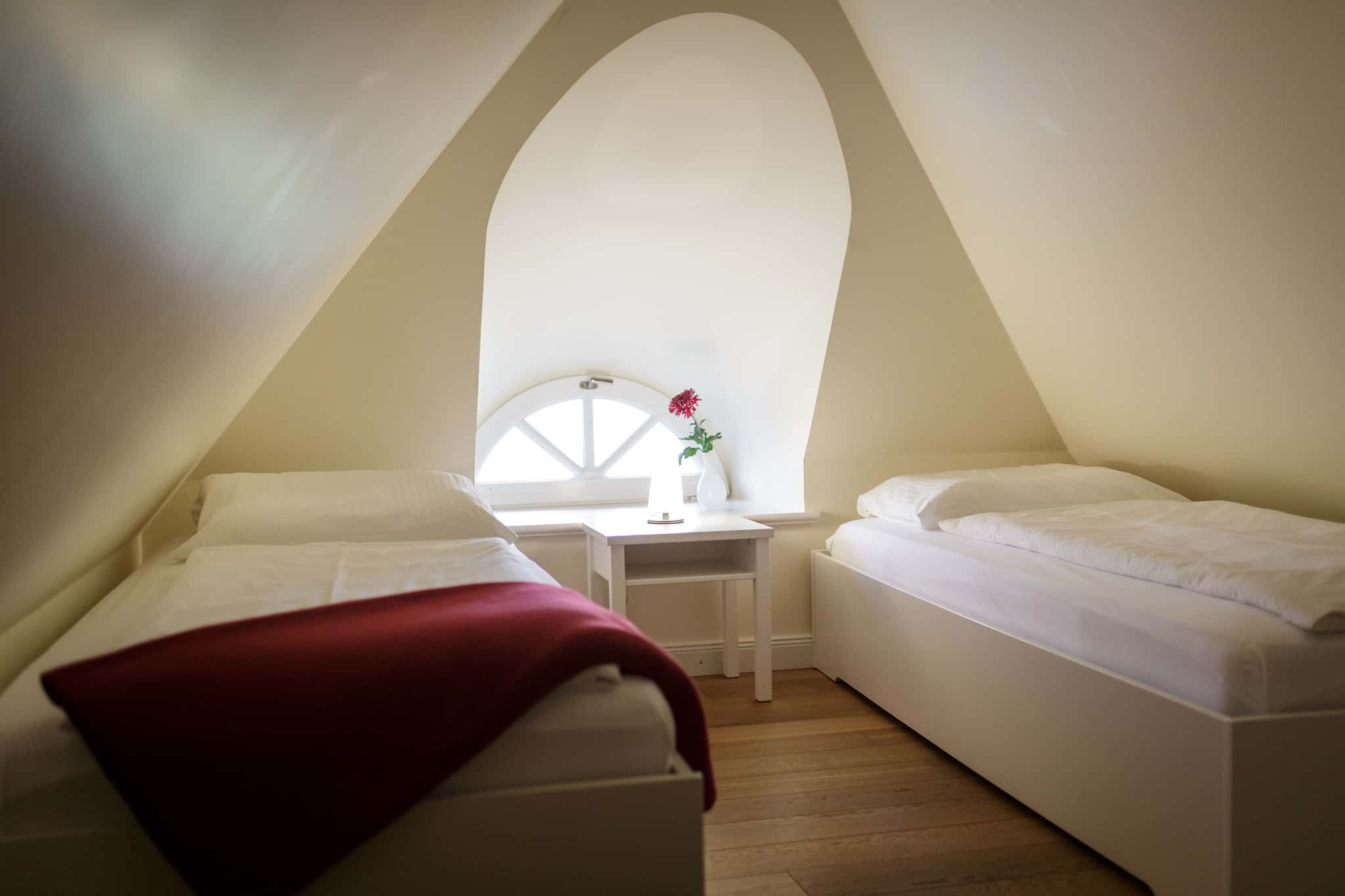 Schlafzimmer mit zwei Einzelbetten unter der Dachschräge und Rundbogenfenster, Appartement Weidenröschen