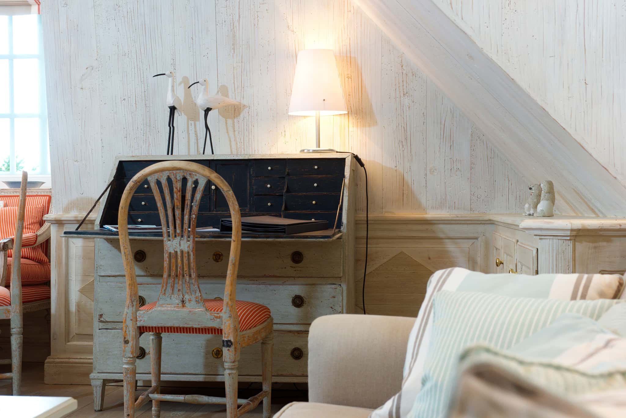 Weißer Sekretär mit Stuhl, Lampe und Holzvögeln an holzvertäfelter Wand in der Ferienwohnung Tipkenhoog